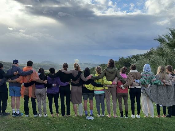 Eine Gruppe steht Arm in Arm auf einer Wiese und schaut über das Tal