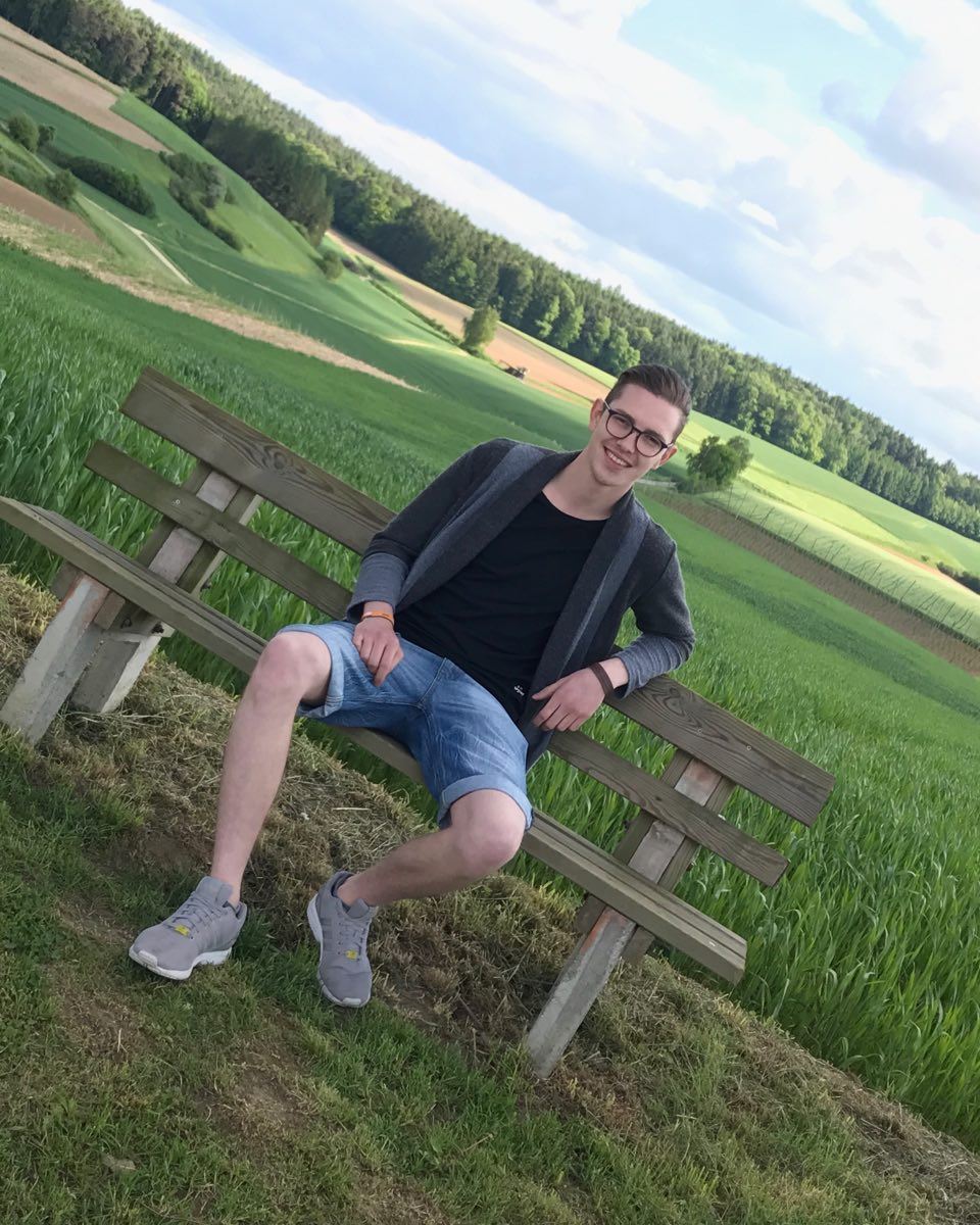 Franz sitzt auf einer Holzbank zwischen grünen Feldern